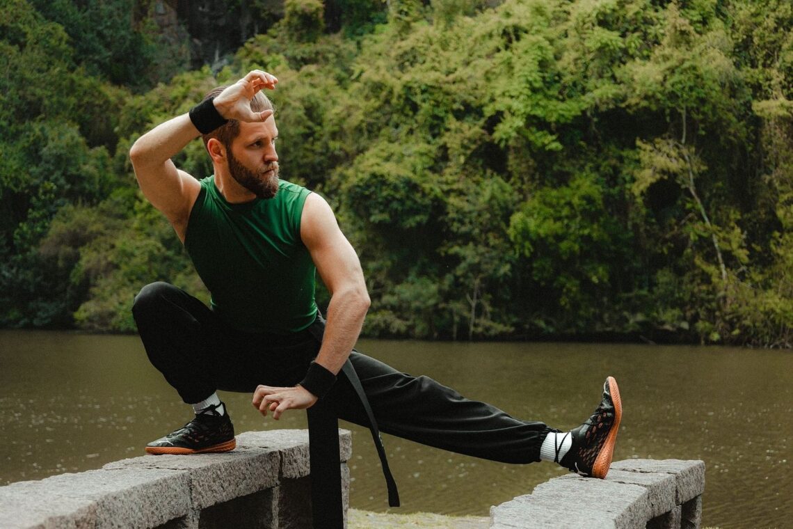 Athlete practicing a low, extended-leg balance stance beside a forested lake
