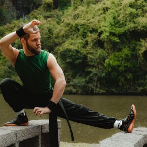 Athlete practicing a low, extended-leg balance stance beside a forested lake
