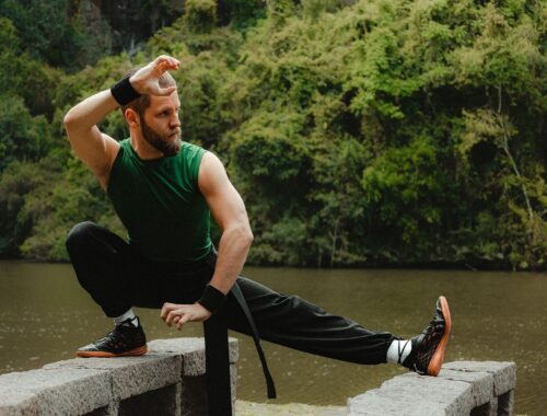 Athlete practicing a low, extended-leg balance stance beside a forested lake