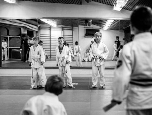 Young martial arts students stand on a matted floor facing an instructor