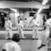 Young martial arts students stand on a matted floor facing an instructor