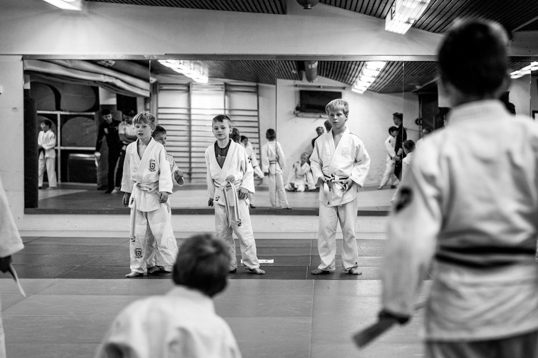 Young martial arts students stand on a matted floor facing an instructor