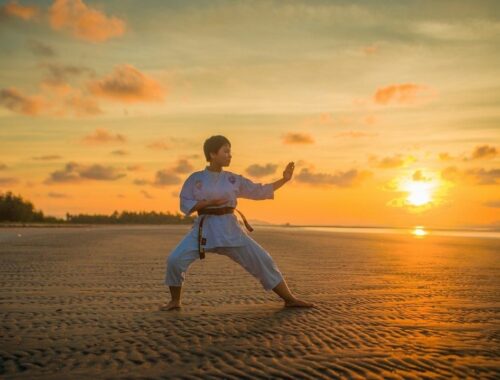 Adult martial artist practicing a stance on a beach at sunset