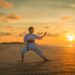 Adult martial artist practicing a stance on a beach at sunset