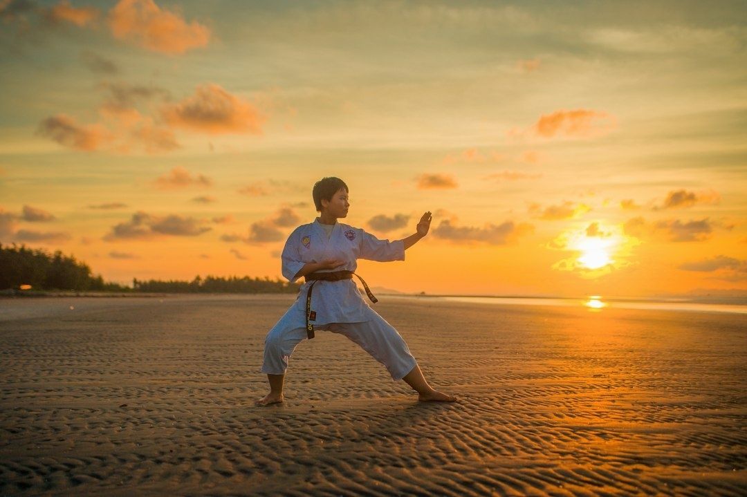 Adult martial artist practicing a stance on a beach at sunset