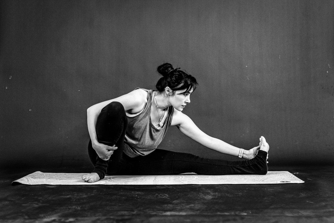 Black-and-white image of a woman performing a seated leg stretch on a mat